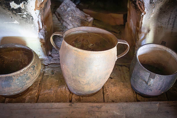 Three old pots sit on a wooden shelf, one of which is a large, rusty pot. The other two are smaller, and they all appear to be old and worn. The scene gives off a sense of nostalgia and history