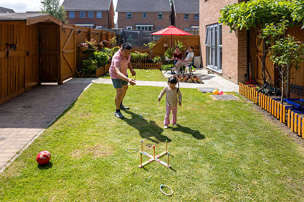 Wide high angle shot of a multi generation family playing games together in their back garden in summer time. They live in Newcastle Upon Tyne, North East England. A grandfather is teaching his young granddaughter how to play ring toss.Videos are available similar to this scenario.