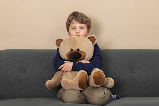 istock Autism concept. Lonely little boy with teddy bear on sofa at home 2224066218