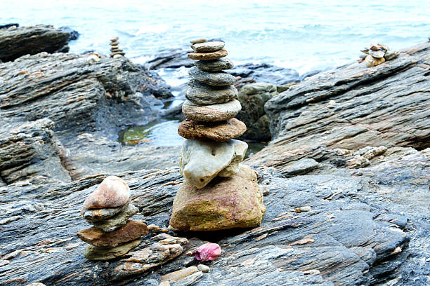 Balanced stone piles on rocky seashore with ocean waves in background. Symbol of mindfulness, stability, and peaceful natural scene.