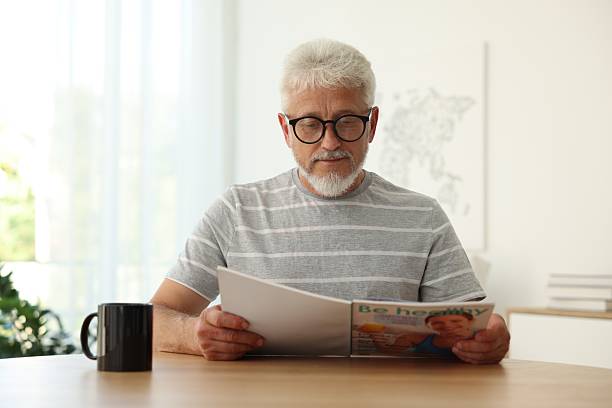 istock Senior man reading magazine at table indoors 2224069040