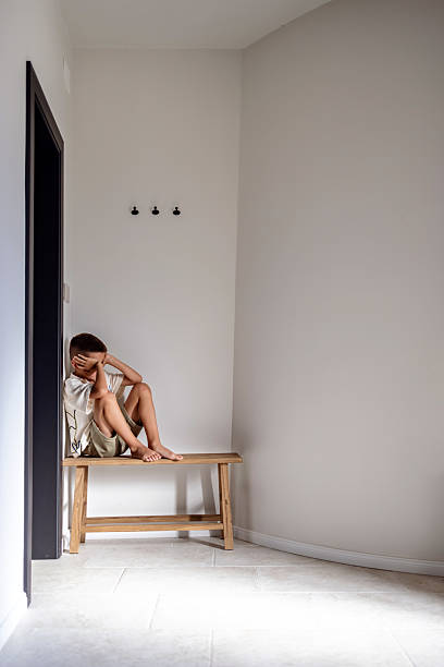 istock Lonely Child Sitting on Bench in Minimal Empty Room Corner 2224072550
