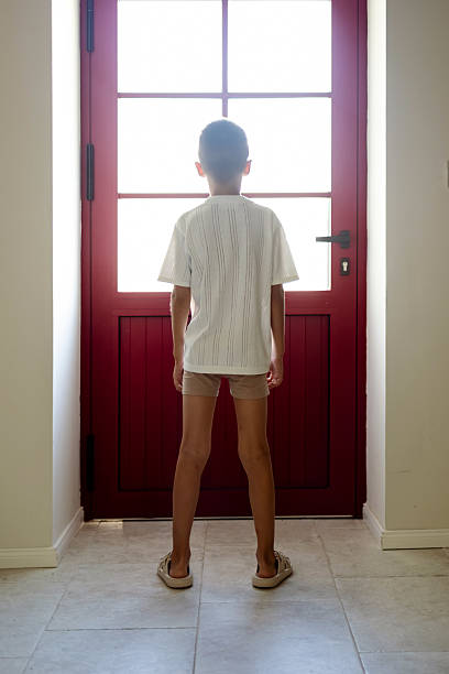 istock Boy Standing Inside Facing Bright Light Through a Red Glass Door 2224072601