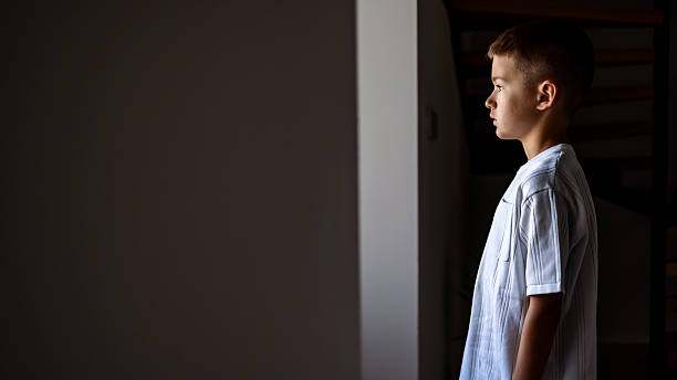 istock Young Boy Standing Indoors in Soft Lighting and Thoughtful Expression 2224072634