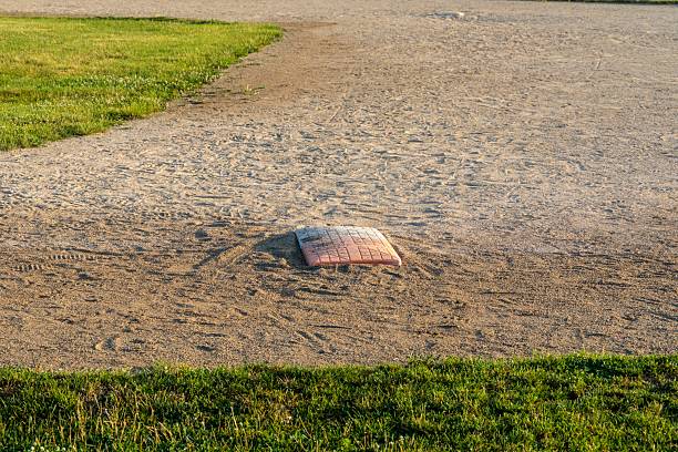 this photo is of a Baseball Player Running to third base on Baseball Field during Baseball Game. the third base is white. and infield of the baseball field is dirt with green grass in the outfield and foul line. the baseball player or athelete is running to third base during a live professional baseball game or little league baseball game. the lighting is natural sunlight during the afternoon or evening. this photo was taken at a live baseball game or sporting event. 