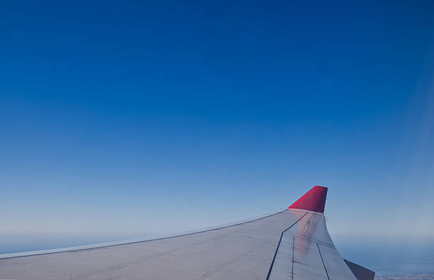 istock A view from an airplane window showing the aircraft's wing with a red tip, flying high above the sea under a clear blue sky 2224074502