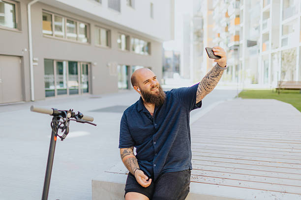 istock Cheerful young man taking selfie on smart phone while sightseeing city on push-scooter 2224076369