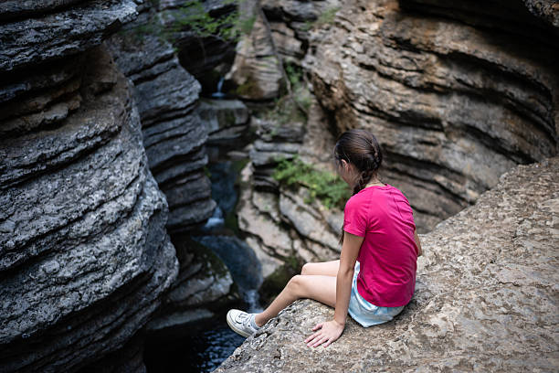 Girl enjoying the breathtaking view of a waterfall cascading through a narrow canyon, embracing the tranquility of nature during her hike