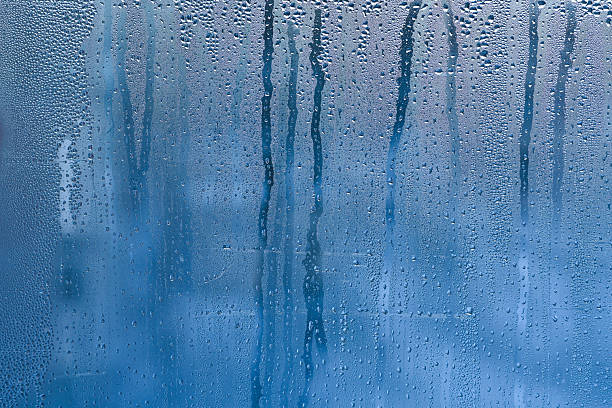 istock condensation, its translucent blue surface with countless micro-droplets. Some droplets grow heavy to begin their slow descent, leaving trails through fogged surface. abstract wet glass background 2224079074