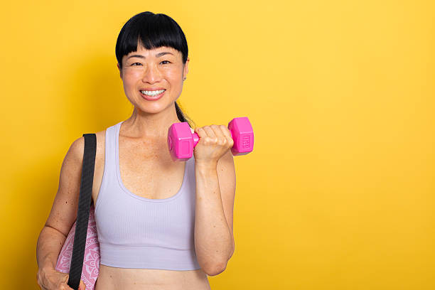 istock Active Lifestyle – Woman Training with Hand Weights on Yellow Background, looking at camera 2224091847