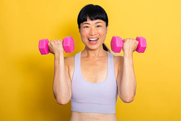 istock Active Lifestyle – Woman Training with Hand Weights on Yellow Background, looking at camera 2224091859