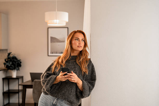 Woman contemplating while holding smartphone in cozy modern interior