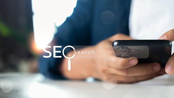 istock Close-up of a hand using a smartphone with an SEO search icon on a virtual search bar, representing mobile search engine optimization, digital marketing, and online business strategy. 2224099739