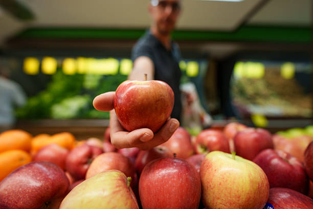 Selective focus on red apples in a market stall, a man choosing one.