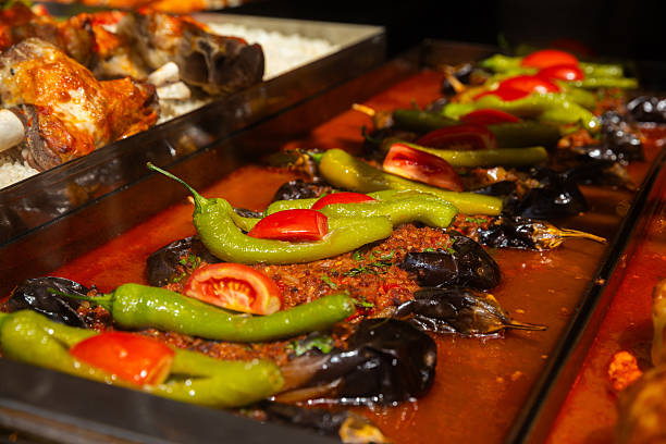A close-up of a traditional Turkish eggplant dish, beautifully arranged in a lokanta (local eatery). The eggplants are generously stuffed and topped with sliced green peppers and tomatoes, all bathed in a rich tomato-based sauce. The warm colors and textures evoke the essence of homemade Anatolian cooking. Ideal for food blogs, travel content, menus, or cultural editorials focusing on Mediterranean or Middle Eastern cuisine.
