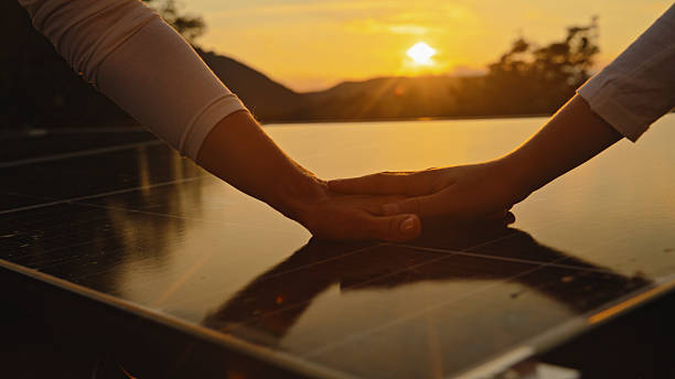 Close-up of a mother and daughter?s hands on a reflective solar panel at sunset, symbolizing unity, sustainability, and renewable energy in a serene outdoor setting.