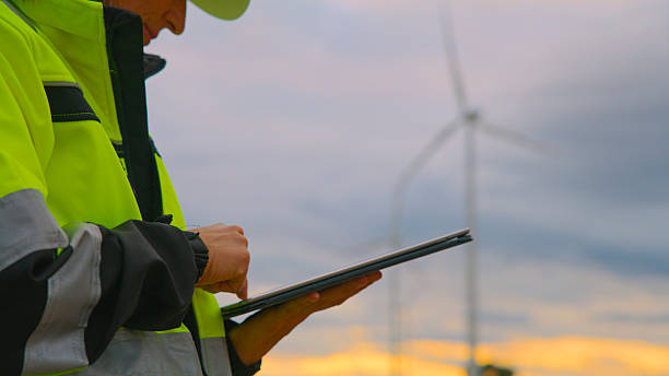 istock Female Engineer in High-Visibility Jacket Using Digital Tablet at Wind Farm During Sunset 2224108190