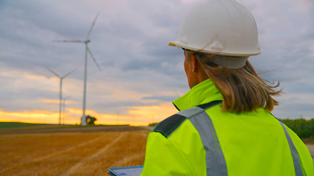 istock Female Engineer Analyzing Wind Turbines Efficiency Outdoors at Sunset Wearing Safety Gear 2224108195