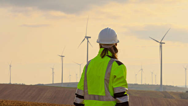 istock Female Engineer in High-Visibility Gear Inspecting Wind Power Farm at Sunset 2224108213