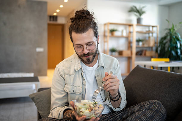 istock Young man eating a fresh salad at home 2224108731