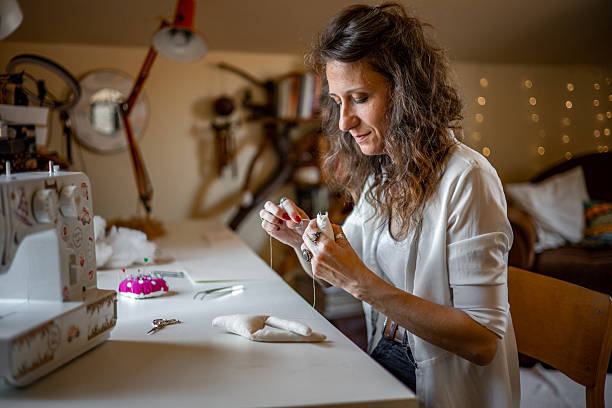 istock Self-employed craftswoman sewing fabric dolls in a charming, light-filled studio, focused on fulfilling bespoke orders for her handmade toy business 2224109516