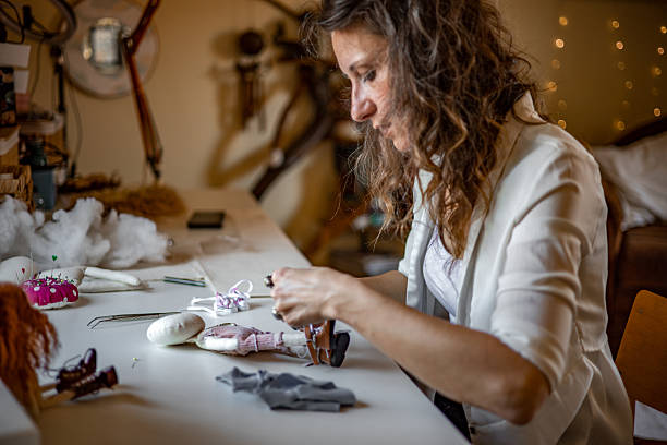 istock Creative female artisan designing and sewing handmade textile dolls in her warm, inviting craft studio — preparing unique pieces for customer orders 2224109601