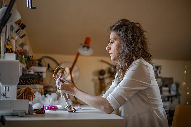 istock Self-employed craftswoman sewing fabric dolls in a charming, light-filled studio, focused on fulfilling bespoke orders for her handmade toy business 2224109847