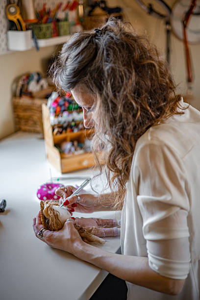 istock Female craft entrepreneur meticulously assembling soft cloth figurines by hand in her intimate maker studio, completing commissioned designs for niche clients 2224109895