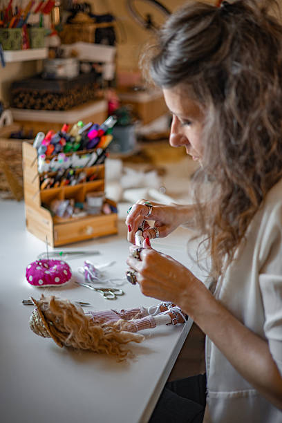 istock Woman entrepreneur working in her home atelier, cutting patterns and sewing charming cloth dolls by hand, fulfilling custom orders for her small business 2224109928