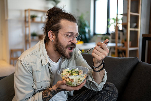 istock Young man eating caesar salad at home on sofa 2224110390