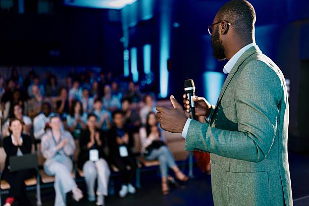 Professional speaker presenting on stage to a diverse audience at a tech event.