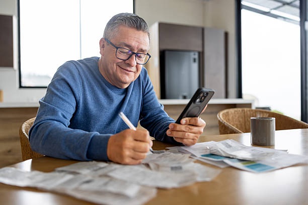 Happy Latin American man paying bills online using his cell phone and smiling - financial planning concepts