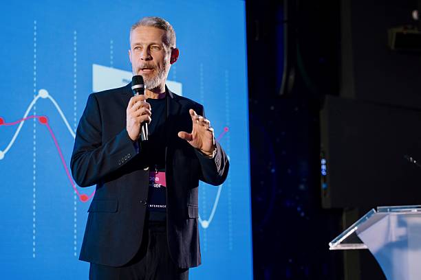 istock Confident Speaker Delivering Keynote at Technology Conference With Visuals on Stage 2224113036