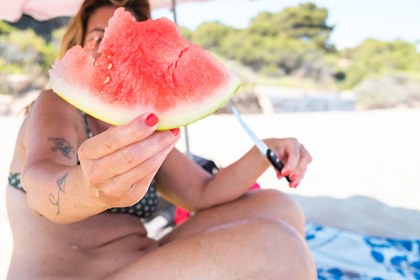 Tourist savoring a juicy slice of watermelon while lounging on a sunny beach, capturing the spirit of summer relaxation and healthy living amidst a vibrant seaside setting