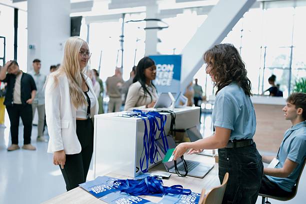 istock Event attendees interacting with staff at a sleek check-in desk featuring badges and technology. 2224118689