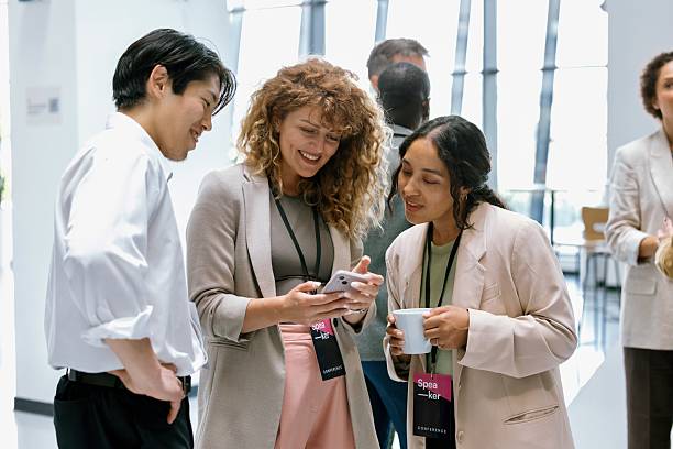 istock Diverse business colleagues sharing smart phone while discussing after conference event 2224118987