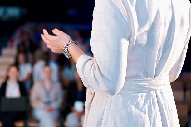 istock Rear View of Presenter Speaking on Stage with Hand in Focus 2224120290