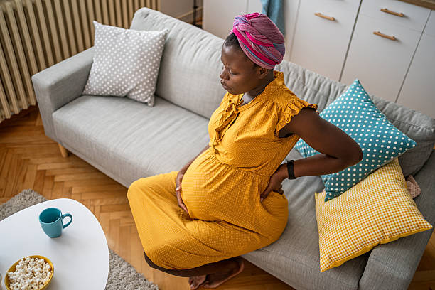 istock Pregnant woman holding her back while sitting on the sofa 2224121931