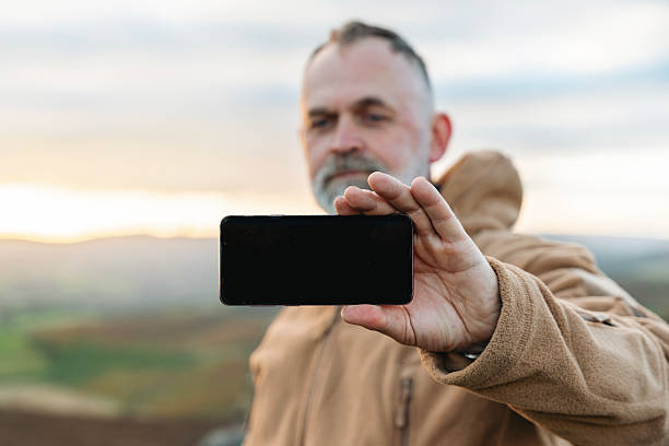 istock Man holds smartphone while standing on a hilltop during sunset in an outdoor landscape, capturing a memorable moment with scenic background 2224126443