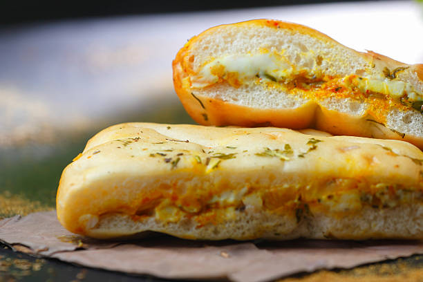 Delicious Indian stuffed paneer kulcha, sliced open to reveal spicy cottage cheese filling, placed on brown paper with scattered herbs.