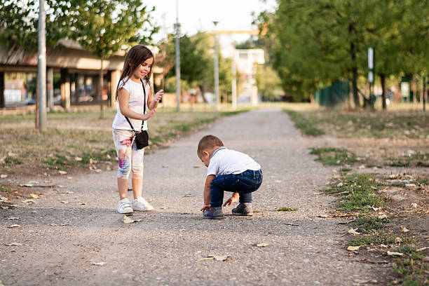 Girl playing joyfully with her baby brother in a park, enjoying the warmth of a beautiful summer day filled with laughter and fun