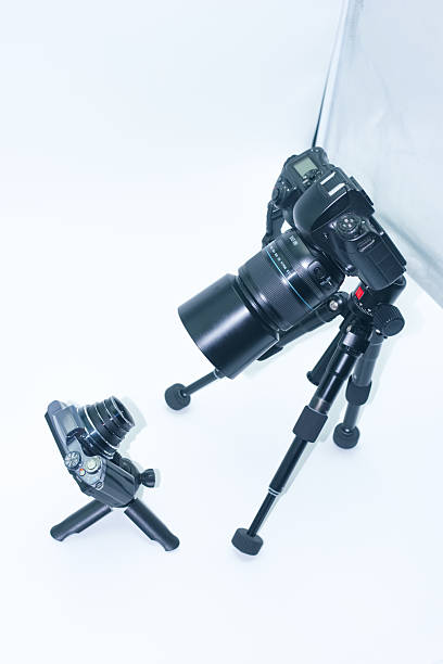 A professional camera is mounted on a sturdy tripod, while a compact camera rests on a mini tripod nearby. The smooth, white backdrop enhances the photography environment.