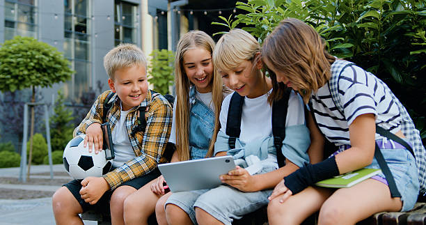 istock Happy boys and girls together use tablet device, smiling while walking sitting on bench after school classes. Back to school. Concept of friendship schoolchildren 2224143123