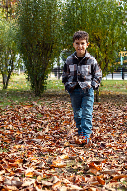 Boy walking over autumn leaves wearing autumn clothes.