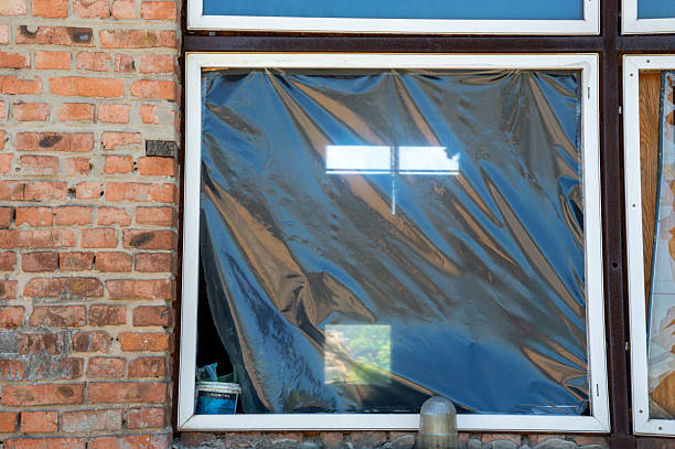 istock Black plastic covers a window, hinting at ongoing renovations in an urban environment, while light reflects off the surface 2224144600