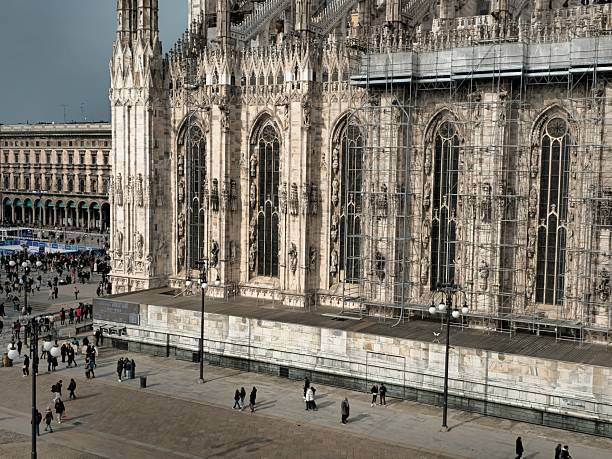 A straight-on, imposing view of the Milan Cathedral's intricately carved white marble facade, showcasing its countless spires, ornate details, and grand entrances against a brilliant blue sky.