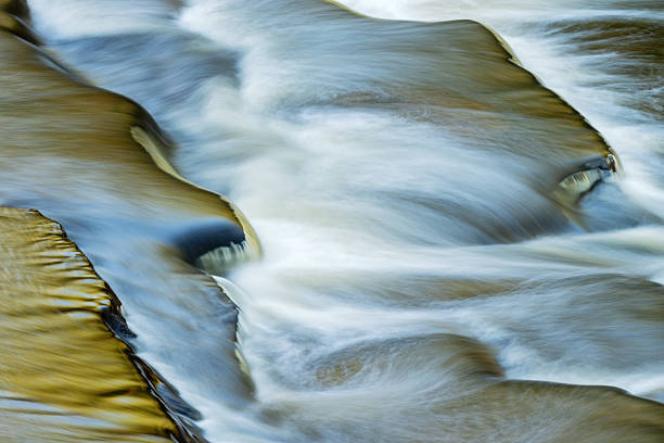 Landscape of the Presque Isle River rapids captured with motion blur and illuminated by reflected color from sunlit foliage and blue sky overhead, Porcupine Mountains Wilderness State Park, Michigan, USA
