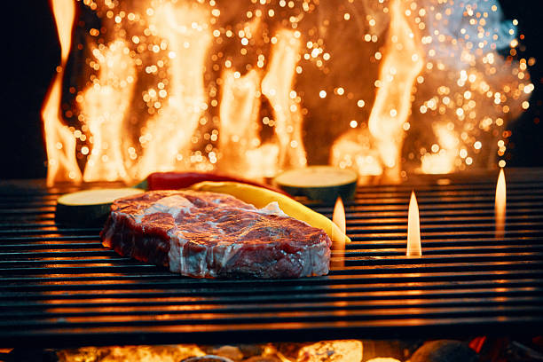 Close-up view of a perfectly grilled steak being flipped over burning wood on an open flame. The glowing embers and dancing flames add warmth and authenticity, capturing the essence of outdoor cooking and smoky flavors.
