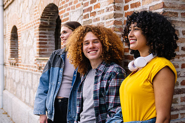 istock Young friends smiling and leaning against a brick wall 2224152101