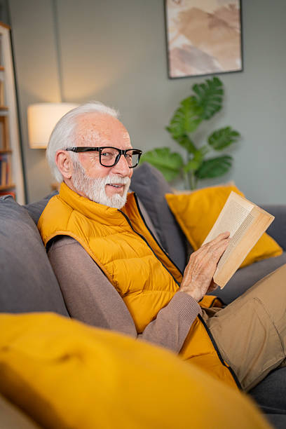 istock Senior man relaxing on sofa reading a book and smiling 2224154525